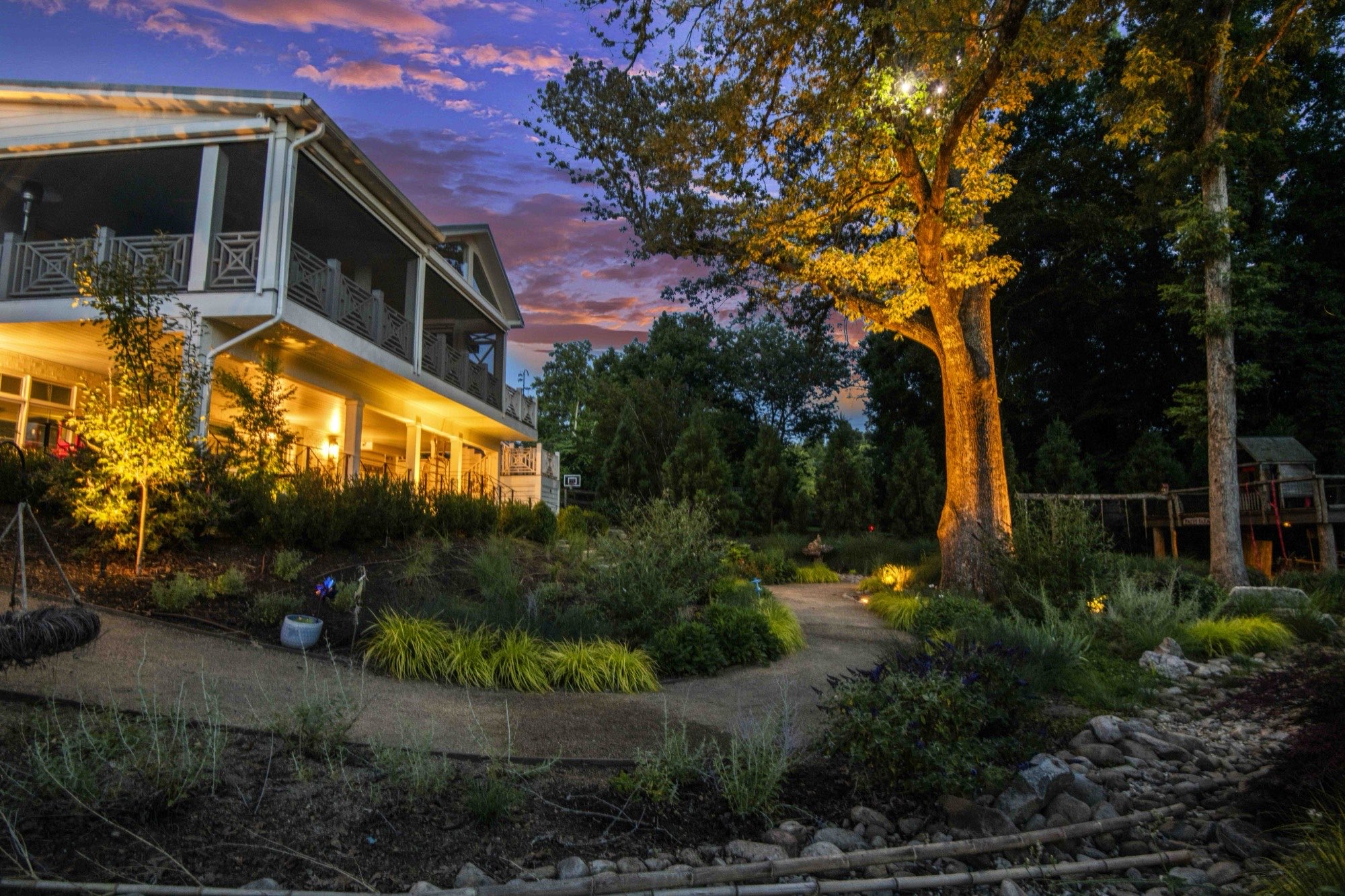 Renovated hillside home and gardens glowing at twilight under a purple sky