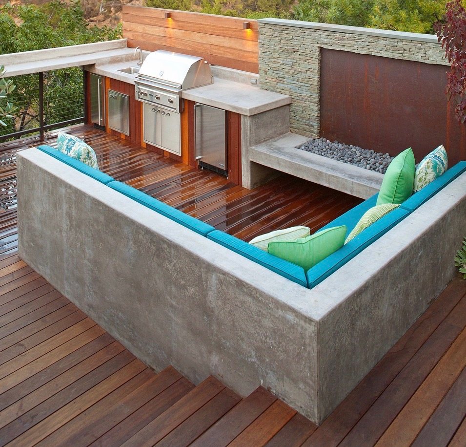 Poured-concrete sunken seating wrapped around a hardwood deck with an outdoor kitchen and fire feature