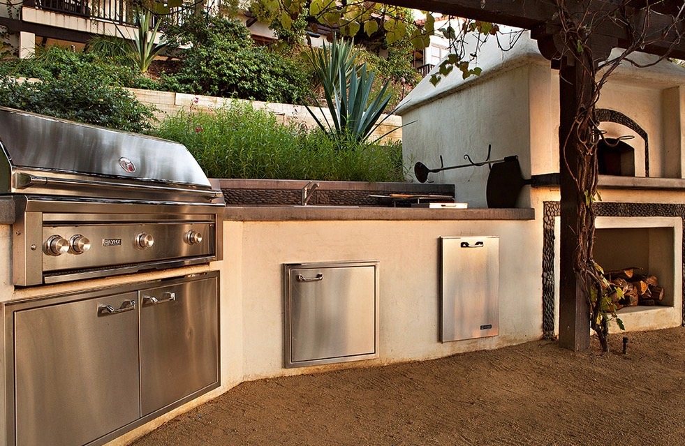 Stainless built-in grill, access doors, and a concrete prep counter with sink set in a stucco base