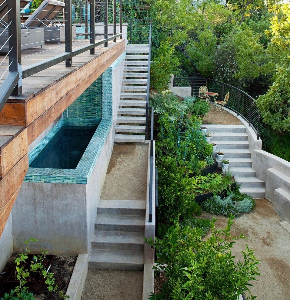 Concrete stairways descending a hillside past a tiled plunge pool and terraced vegetable beds