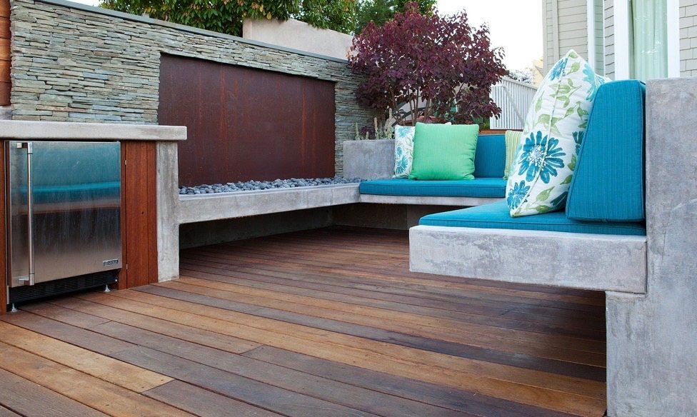Poured-concrete bench with teal cushions beside a linear fire feature and corten-steel wall