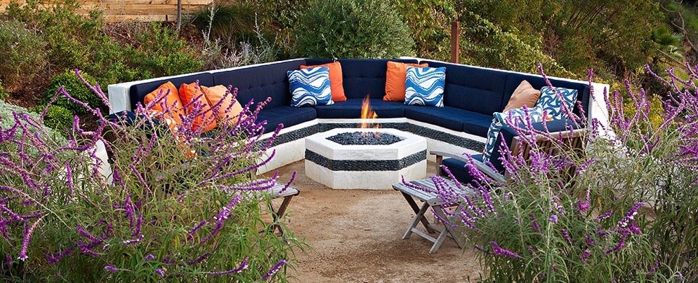 Curved built-in sectional seating around a hexagonal gas fire pit framed by purple salvia