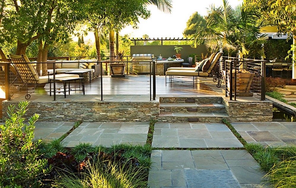 Bluestone patio with grass joints leading up stacked-stone steps to a raised lounge deck