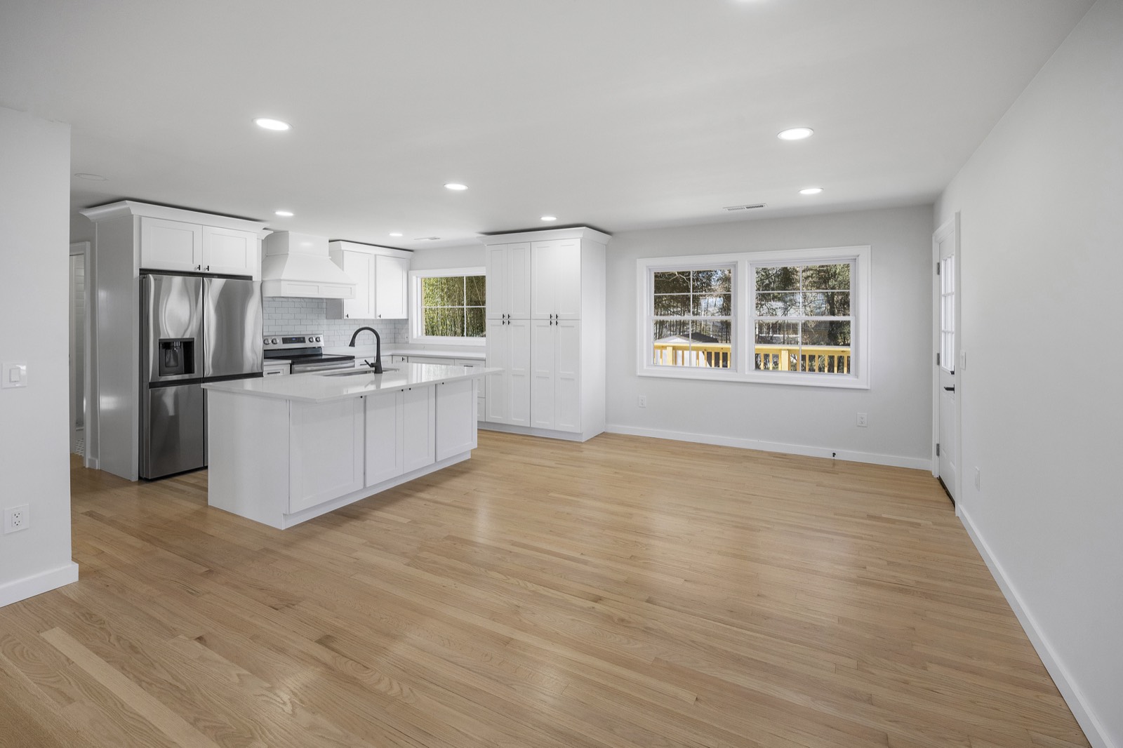 Open-concept white kitchen with island flowing into a light-filled great room