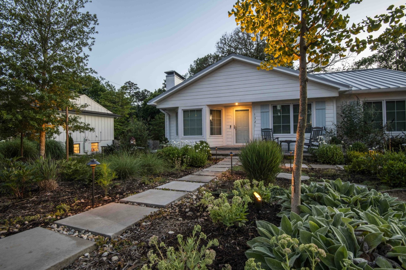 Renovated cottage glowing at dusk behind a layered native front garden