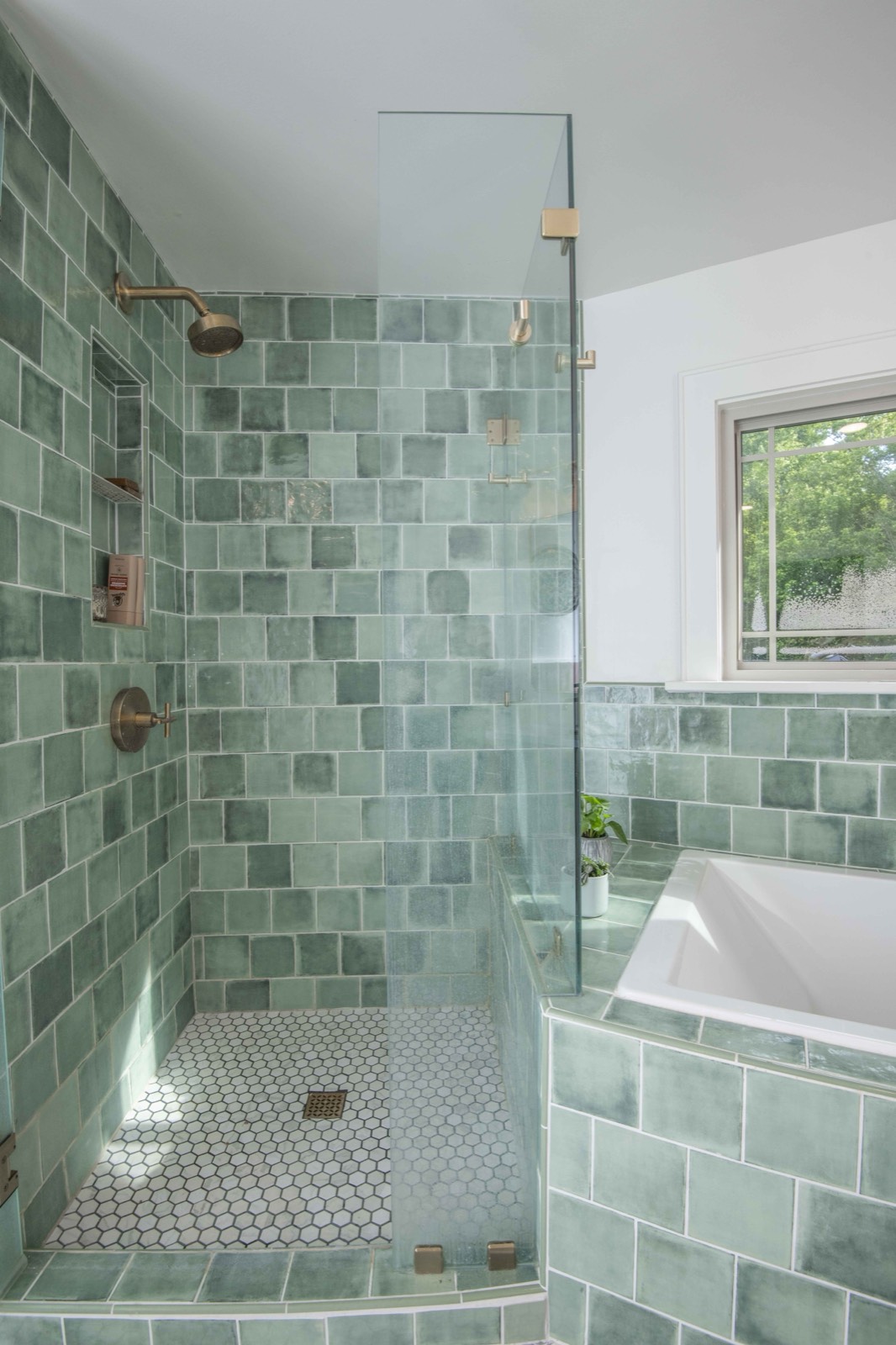 Walk-in shower clad in handmade green tile with a niche and brushed fixtures
