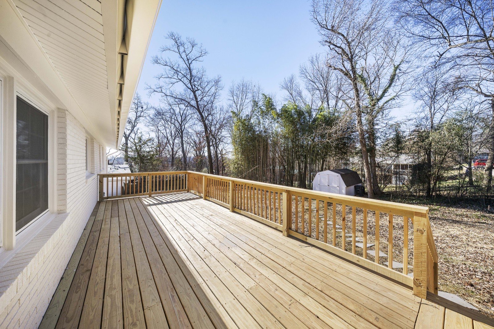 Wide wraparound wood deck with railings overlooking a wooded backyard