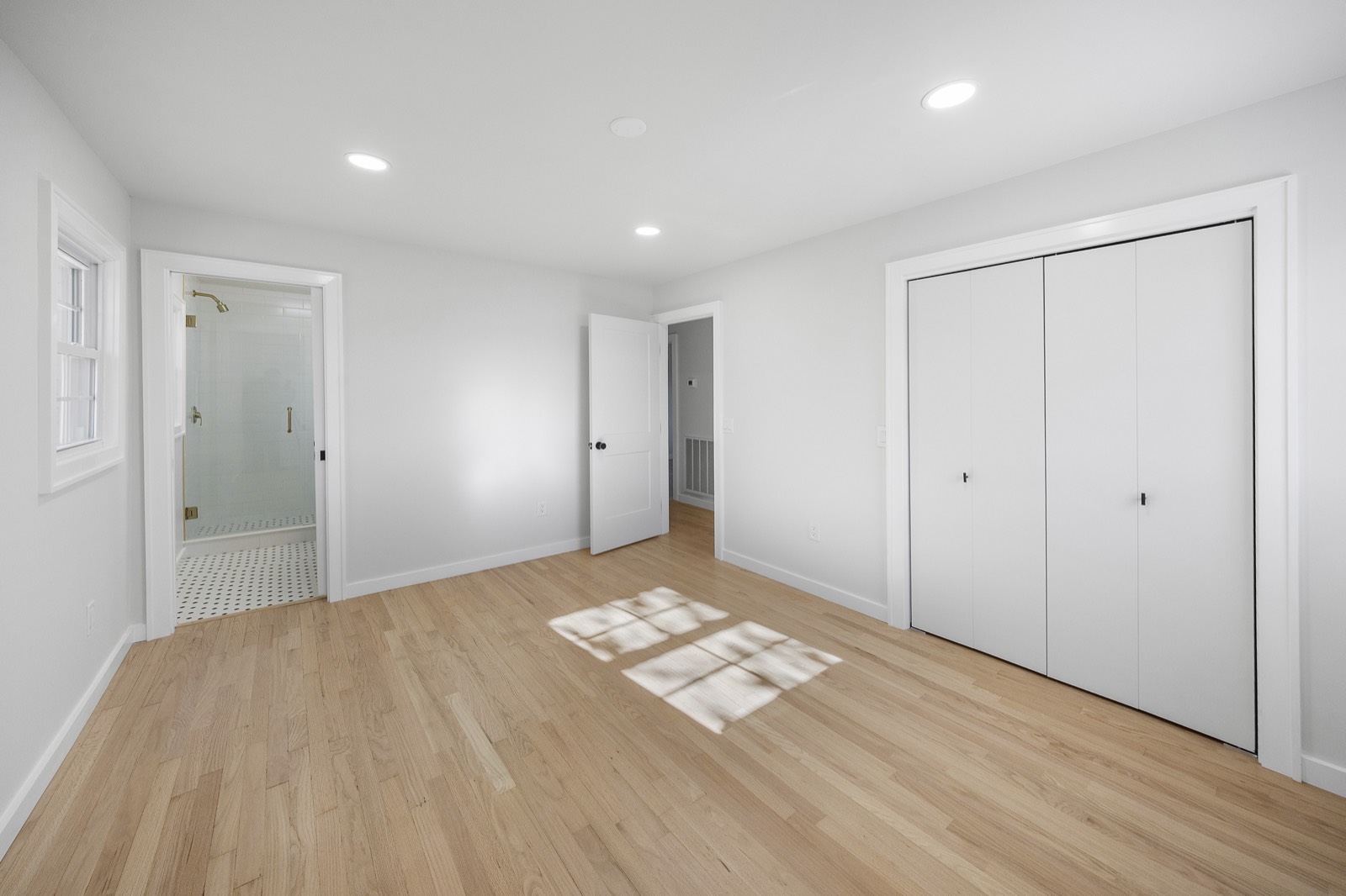 Bright bedroom with oak floors, a double closet, and an ensuite shower