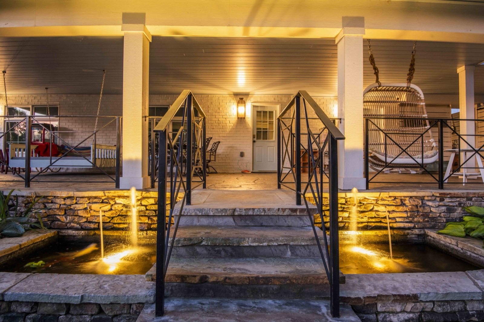 Illuminated covered porch with stone columns above a lit koi pond