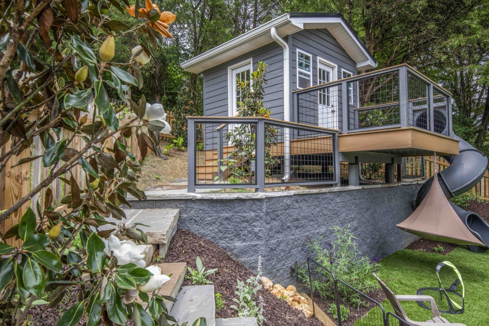 Renovated board-and-batten cottage framed by a deck and layered gardens