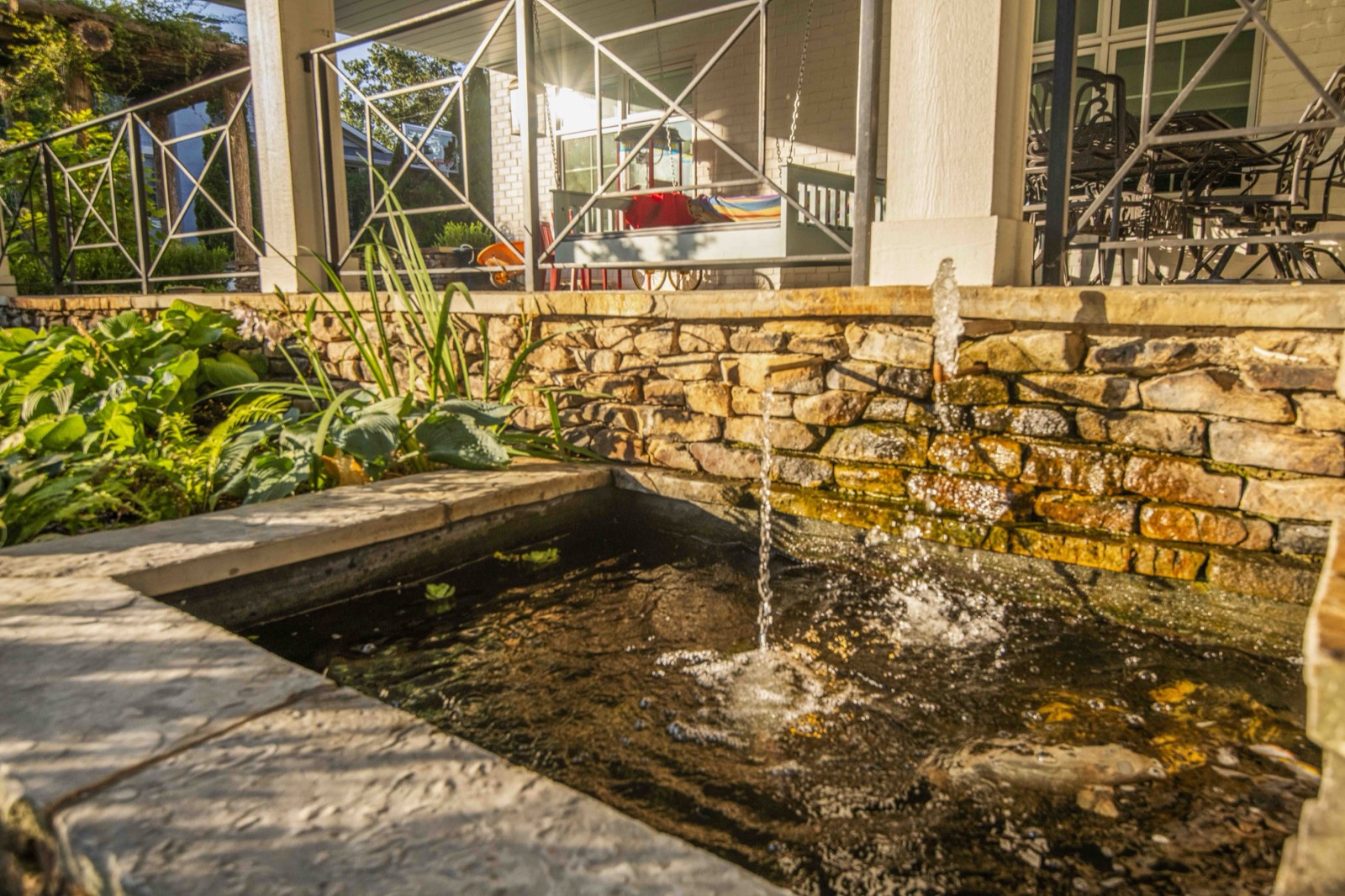 Stone-edged koi pond with a bubbling fountain below the covered porch