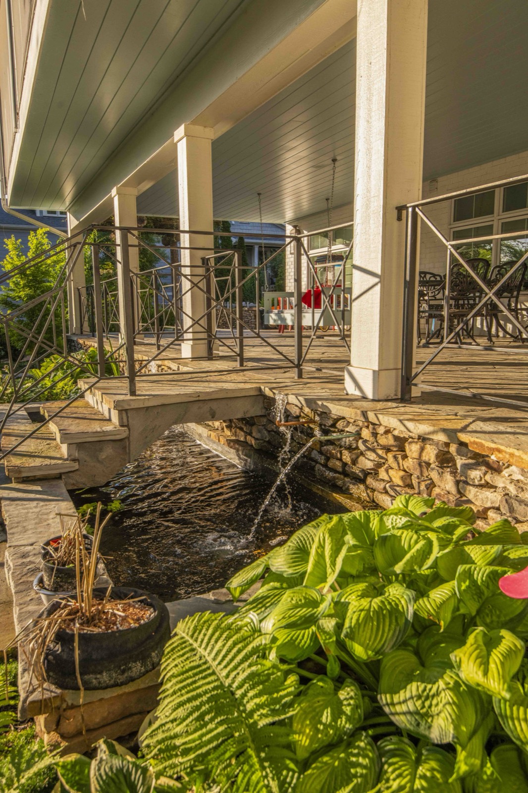 Water channel and fountain running beneath the porch beside lush hostas
