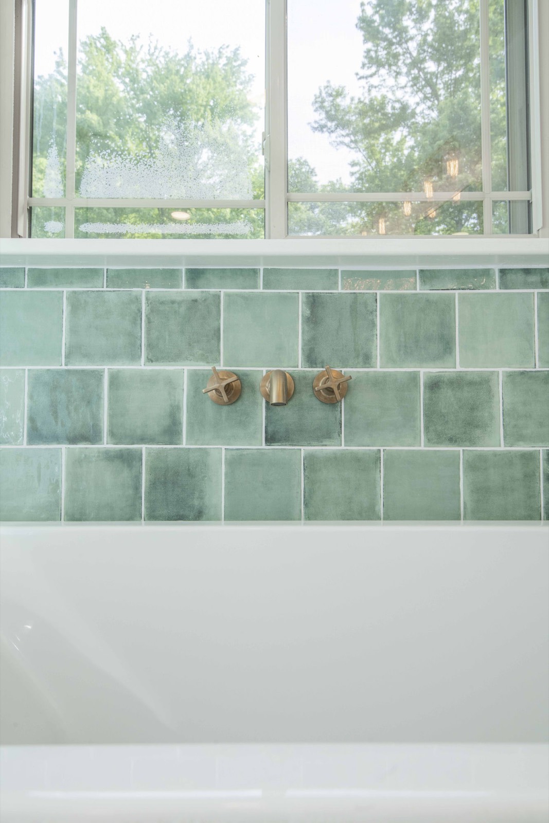 Built-in soaking tub framed by hand-glazed green tile and brass wall fillers