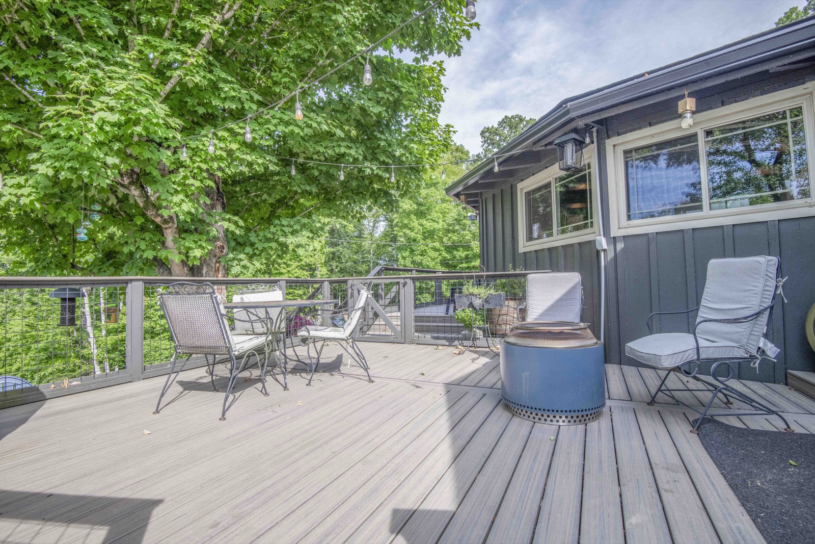 Wraparound deck with bistro seating and a fire pit beneath mature maples