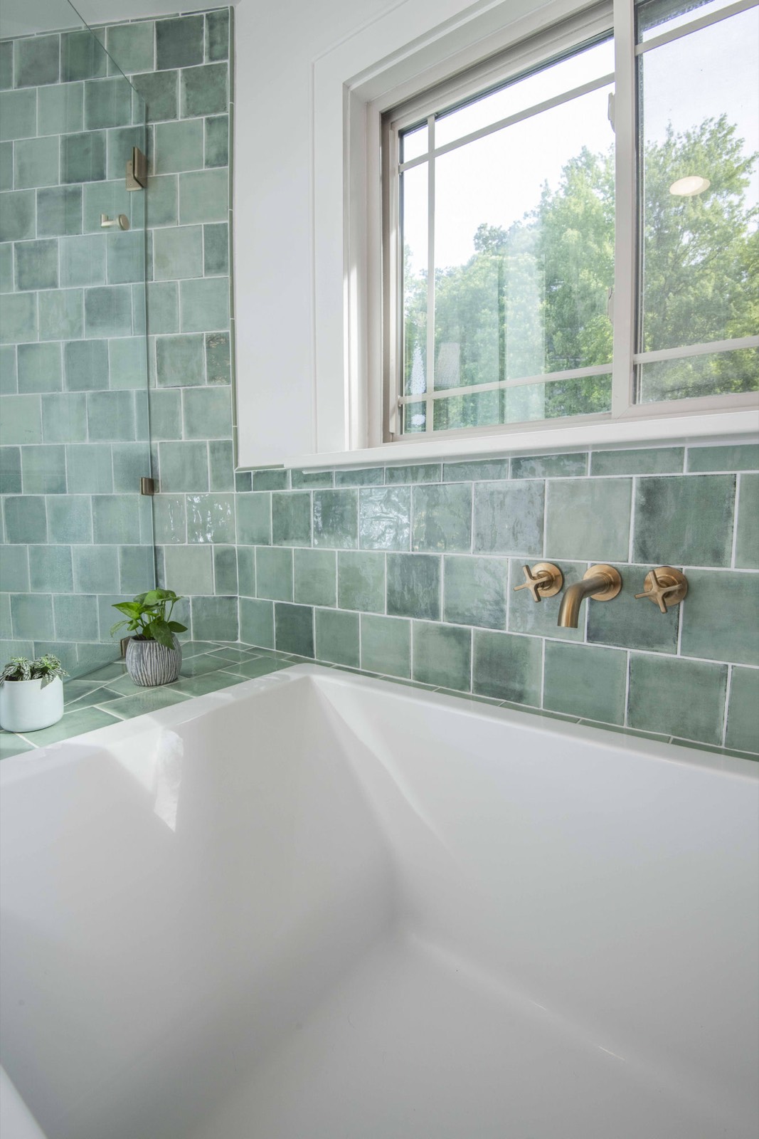 Corner soaking tub with green tile, a picture window, and brass fixtures