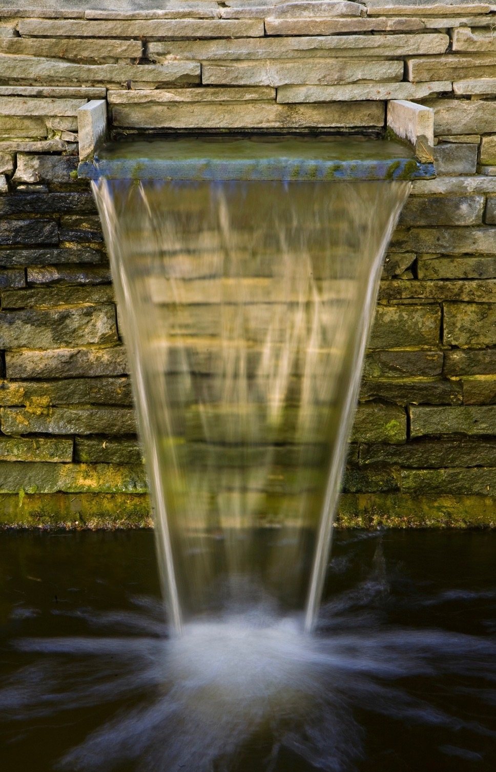 Close-up of a sheet of water falling from a stone scupper set in a dry-stacked wall